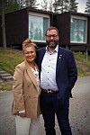 Kaksi ihmistä poseeraa modernin tumman rakennuksen edustalla metsäisessä ympäristössä.