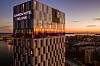 Valaistu Clarion Hotel Helsinki Helsingin iltahämärässä kaupungin yllä.