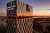 Valaistu Clarion Hotel Helsinki Helsingin iltahämärässä kaupungin yllä.