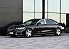 Musta Mercedes-Benz-sedan modernin rakennuksen edustalla.