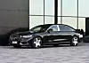 Musta Mercedes-Benz-sedan modernin rakennuksen edustalla.