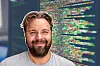 Leende skäggig man framför en datorskärm med färgrik programmeringskod.